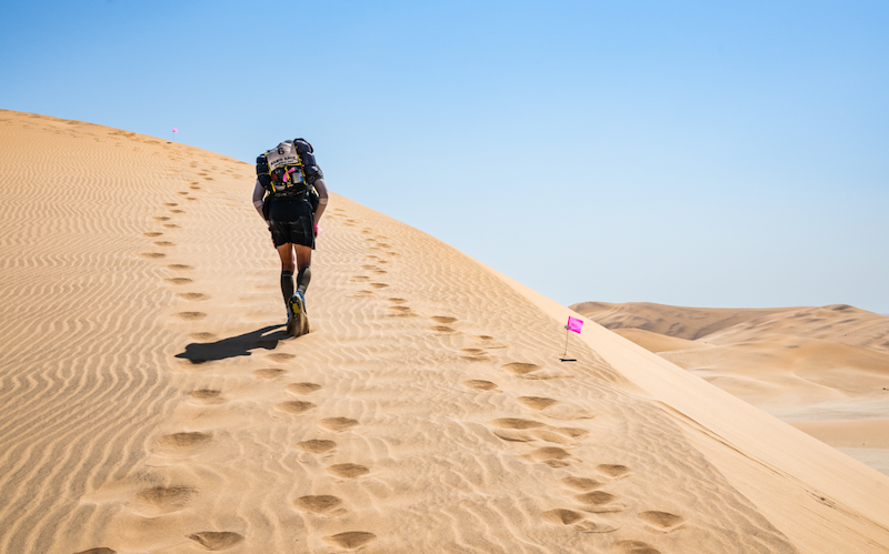 Photo courtesy of Racing the Planet of runner with pack hiking up a sand dune in the middle of the Atacama Desert in Chile